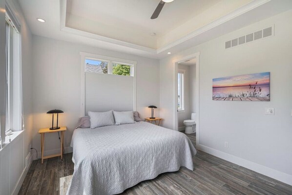 A bedroom with a bed, two bedside tables, a ceiling fan, a window, and a painting on the wall.