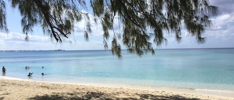 Uma praia com águas turquesa cristalinas, pessoas nadando e uma bolsa na areia.