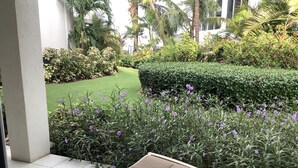 Un espace détente avec un fauteuil confortable, un jardin bien entretenu avec des fleurs violettes et une pelouse impeccable.