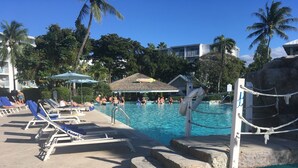 Un espace piscine avec des chaises longues, une structure à toit de chaume et une barrière faite de cordes.