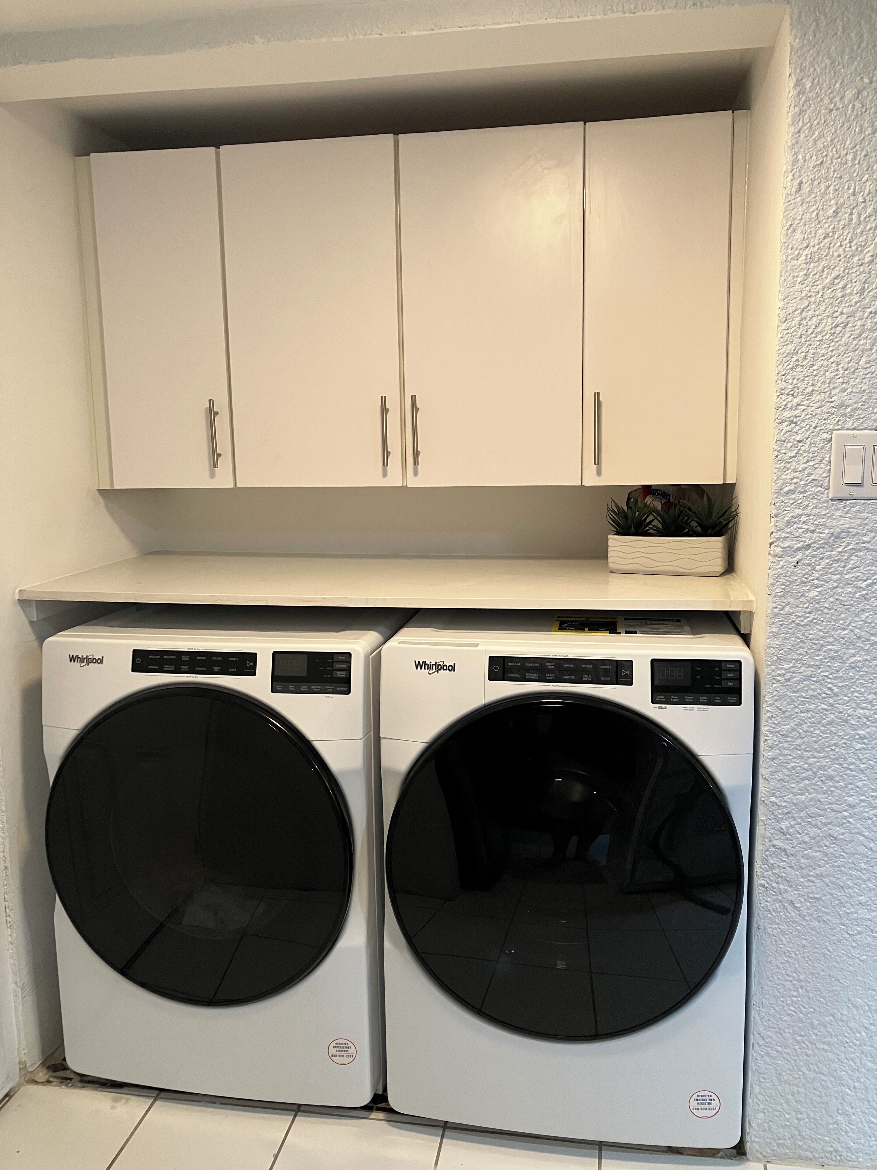 Een wasruimte met twee Whirlpool voorladers en witte kasten erboven.