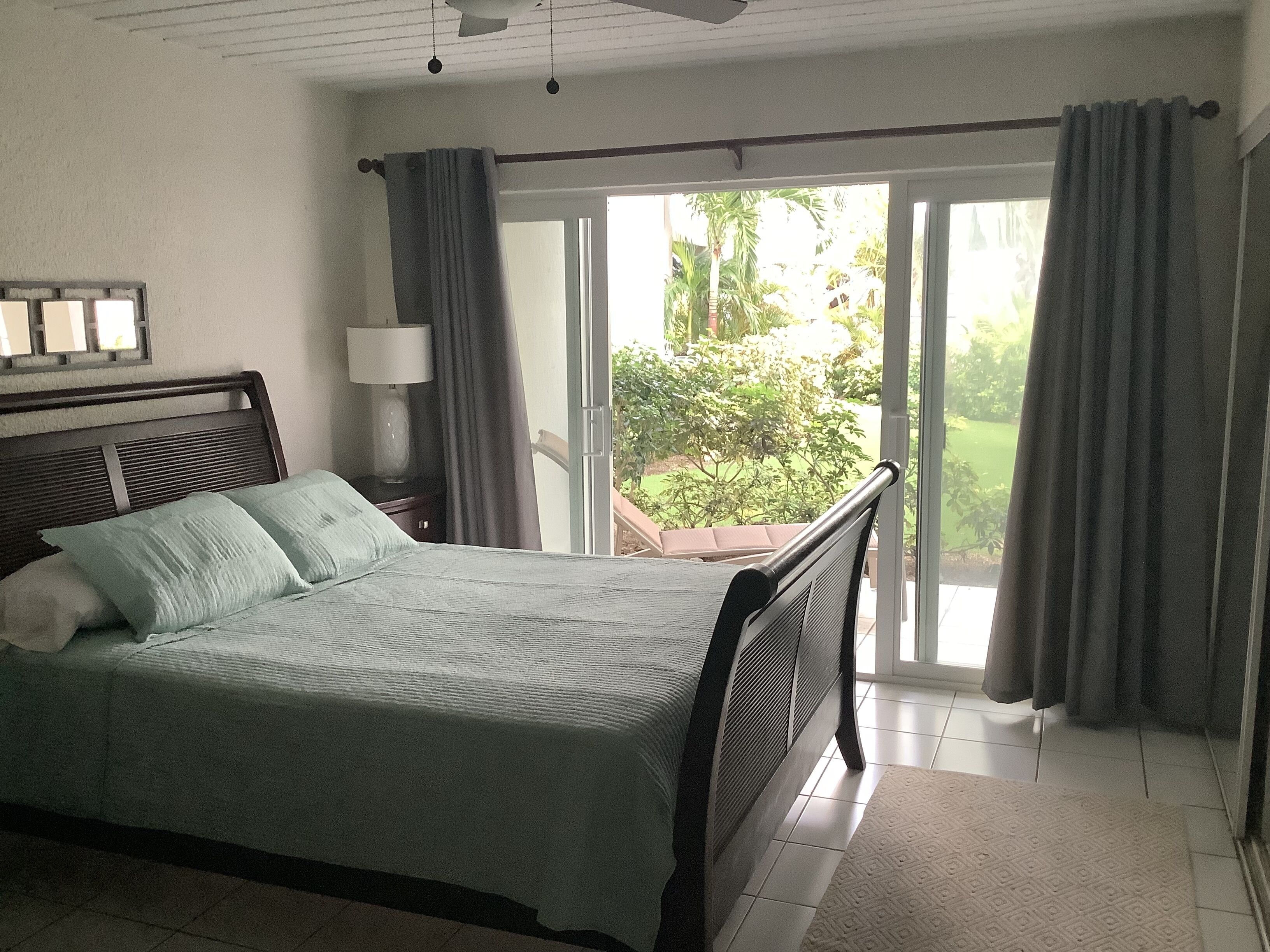 Un dormitorio con cama, mesita de noche, lámpara y vistas a un jardín a través de una puerta corrediza de vidrio.
