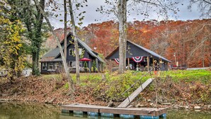 A lakeside cabin with a dock extending into the water, surrounded by autumn foliage and a forest backdrop.
