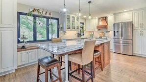 A modern kitchen with white cabinets, a large island with bar stools, stainless steel appliances, and pendant lighting.