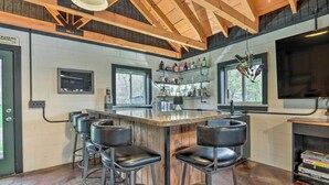 A kitchen with a central island, bar stools, and shelves with bottles.