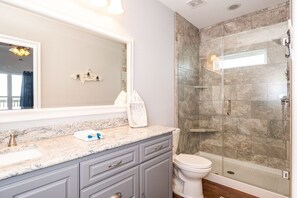 Une salle de bain avec un comptoir en marbre, des toilettes blanches, une douche à parois de verre et un grand miroir.