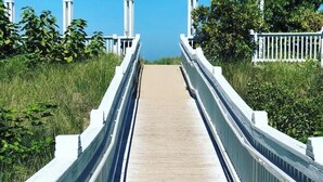 Un paseo marítimo de madera que conduce a una cerca blanca, con una vista despejada del cielo.