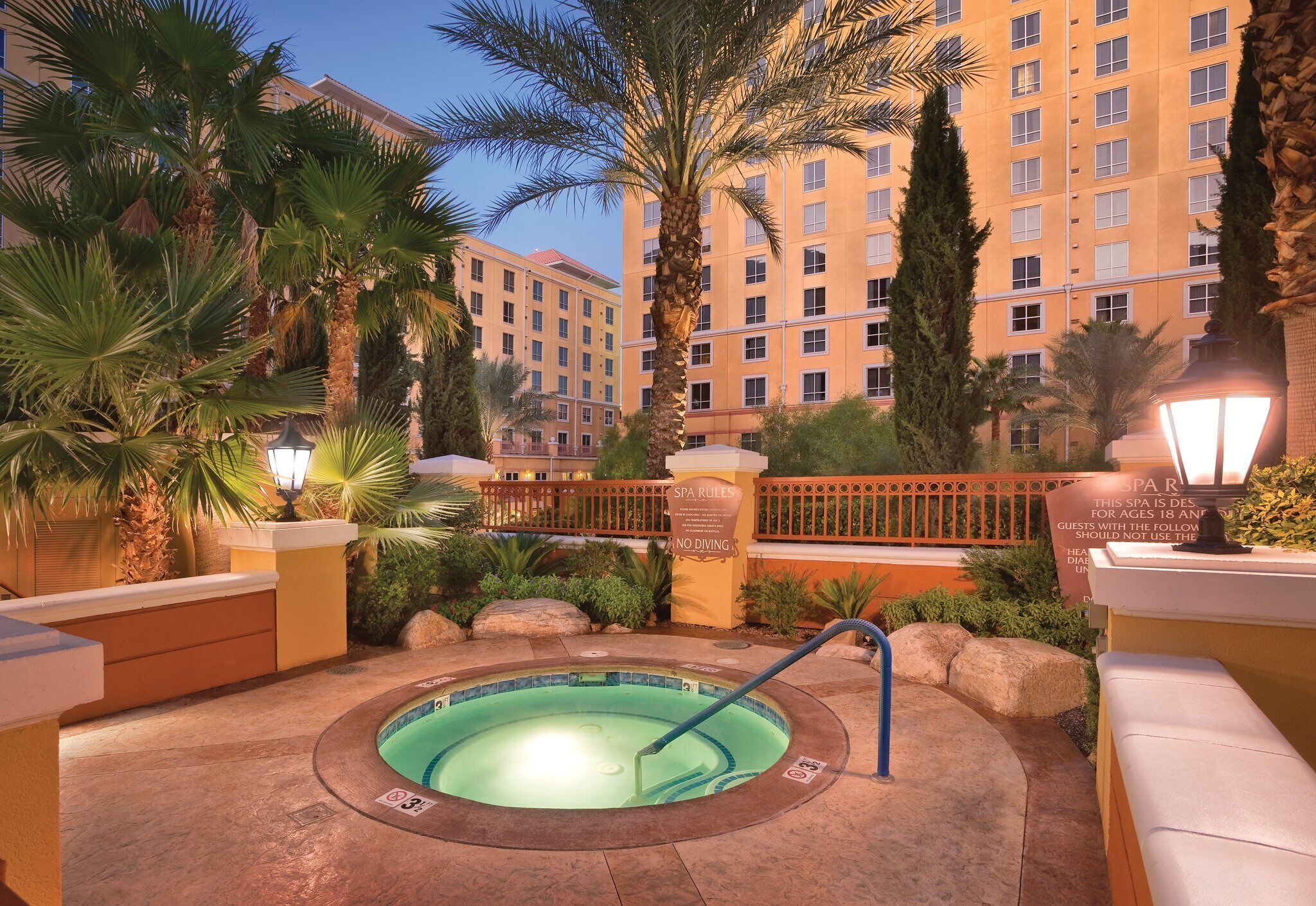 A hot tub surrounded by palm trees and a poolside area with a spa sign indicating age restrictions.