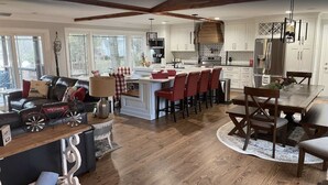 A modern kitchen with white cabinetry, a central island with red chairs, and a dining area with a wooden table and chairs. - Lakefront home with private beach & gourmet kitchen (Sherrills Ford)