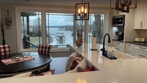 A modern kitchen with a large island, a dining area with checkered chairs, and a view of a lake. - Lakefront home with private beach & gourmet kitchen (Sherrills Ford)