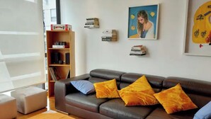 Una sala de estar moderna con un sofá de cuero, cojines coloridos, una estantería y un cuadro en la pared.