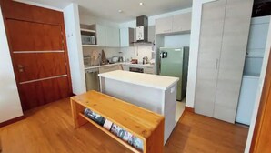 Una cocina compacta con armarios blancos, un banco de madera y un refrigerador empotrado.
