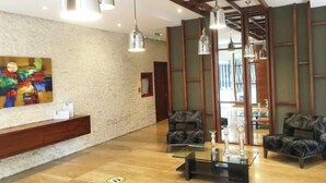 Un vestíbulo amplio con una recepción, dos sillones estampados, una mesa de centro de vidrio e iluminación colgante moderna.
