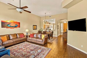 A living room with a sectional sofa, a coffee table, a patterned rug, a ceiling fan, and a painting on the wall.