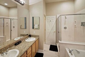Un baño con dos lavamanos, una ducha y una puerta que da a otra habitación.