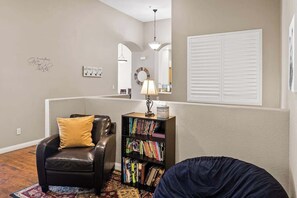 A living room with a black leather chair, a bookshelf, a lamp, and a round mirror.