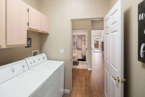 A laundry room with a front-loading washer and dryer, wooden cabinets, and a welcome sign.