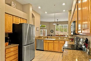 Cocina con gabinetes de madera, refrigerador de acero inoxidable, encimeras de granito y lavavajillas.