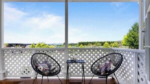 A covered balcony with two black chairs and a small table, overlooking a scenic landscape with trees and distant mountains. - Warm and welcoming, private one bedroom on a lifestyle property. (Waingawa)