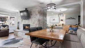 A modern living room with a stone accent wall, a fireplace, a large wooden dining table, and a comfortable seating area.