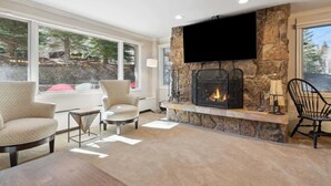 Una sala de estar acogedora con chimenea de piedra, asientos cómodos y grandes ventanales con vistas al exterior.
