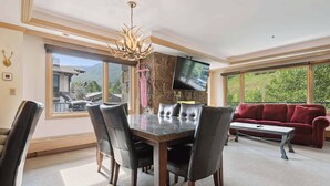 A dining area with a glass table and leather chairs, a red sofa, and a TV on the wall. - Lodge Tower 377 3BR at the base of Vail Mountain (Vail)