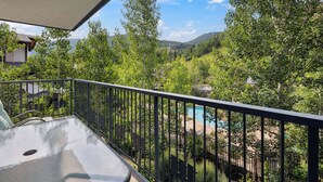 A balcony with a glass table and metal railing, overlooking a swimming pool and lush greenery. - Lodge Tower 377 3BR at the base of Vail Mountain (Vail)
