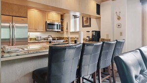 A modern kitchen with stainless steel appliances, wooden cabinets, and a bar area with leather chairs. - Lodge Tower 377 3BR at the base of Vail Mountain (Vail)