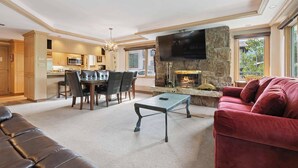 A modern living room with a fireplace, a television mounted on a stone wall, a dining area with a table and chairs, and a leather sofa. - Lodge Tower 377 3BR at the base of Vail Mountain (Vail)