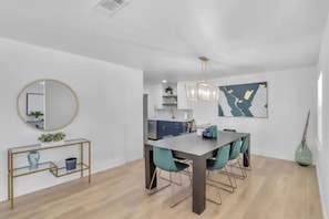 A modern dining area with a wooden table and teal chairs, a round mirror, and a minimalist console table with decorative items. - ☆LakeHouse 4 Bedroom Newly Renovated Heated pool ☆ (Orlando)