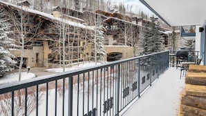 Un balcon enneigé offrant une vue sur une station de ski, avec ses bâtiments et ses arbres.