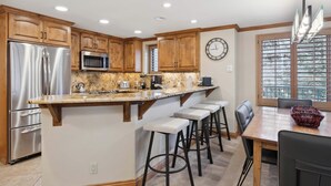 A modern kitchen with wooden cabinets, stainless steel appliances, a marble countertop, and bar stools. - Lodge Tower 277 3BR at the base of Vail Mountain (Vail)