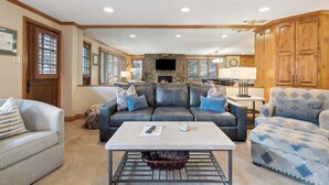 A spacious living room with a large sofa, a coffee table, and a fireplace. There is a kitchen area in the background with wooden cabinets and a dining table. - Lodge Tower 277 3BR at the base of Vail Mountain (Vail)