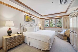 Une chambre à coucher avec un grand lit, une table de chevet avec une lampe, une commode, une chaise et une fenêtre avec des rideaux.