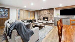 A modern living room with a fireplace, a dining area, and a kitchen with a TV. - Lodge Tower 287 3BR at the base of Vail Mountain (Vail)