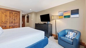 A hotel room with a bed, a dresser, a television, a chair, and wall art. - Lodge Tower 294 2BR at the base of Vail Mountain (Vail)