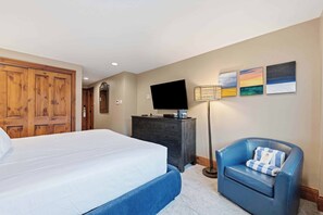 A hotel room with a bed, a dresser, a television, a chair, and wall art.