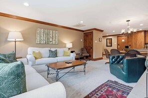 Una sala de estar con sofá, mesa de centro y sillones, un comedor con mesa y sillas, y una cocina con armarios de madera y una araña.