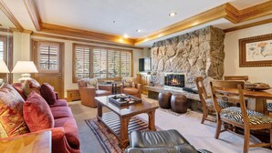 A spacious living room with a stone fireplace, leather furniture, and large windows.