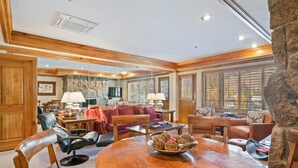 A spacious living room with a wooden dining table, leather chairs, and a red sofa.