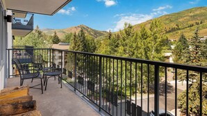 A balcony with a view of a mountainous landscape, a railing, and outdoor furniture.
