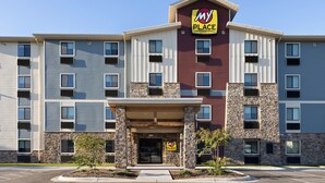 Un hotel de varios pisos con fachada de piedra, un letrero llamativo que dice 'My Place' y un estacionamiento al frente.
