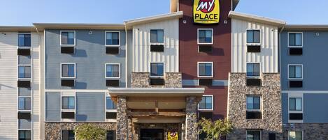 A multi-story hotel with a stone facade, a prominent 'My Place' sign, and a parking lot in front.