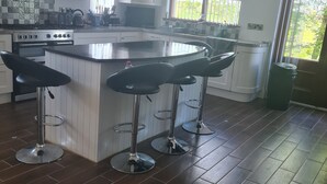 A modern kitchen with a central island, bar stools, and a large window.