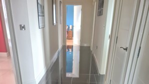 A corridor with glossy black and white tiled floors, white walls, and a door at the end.