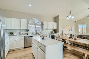 Une cuisine moderne avec des meubles blancs, un îlot central et un coin repas comprenant une table et des bancs en bois.