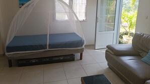 A room with a bed under a mosquito net, a sofa, a door to a balcony, and a painting on the wall. - Le petit coin de campagne  (Le Robert)