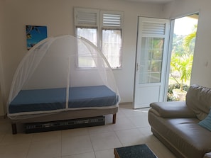 Une chambre avec un lit sous une moustiquaire, un canapé, une porte donnant sur un balcon et un tableau au mur.