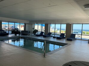 An indoor swimming pool with lounge chairs and a view of the ocean.