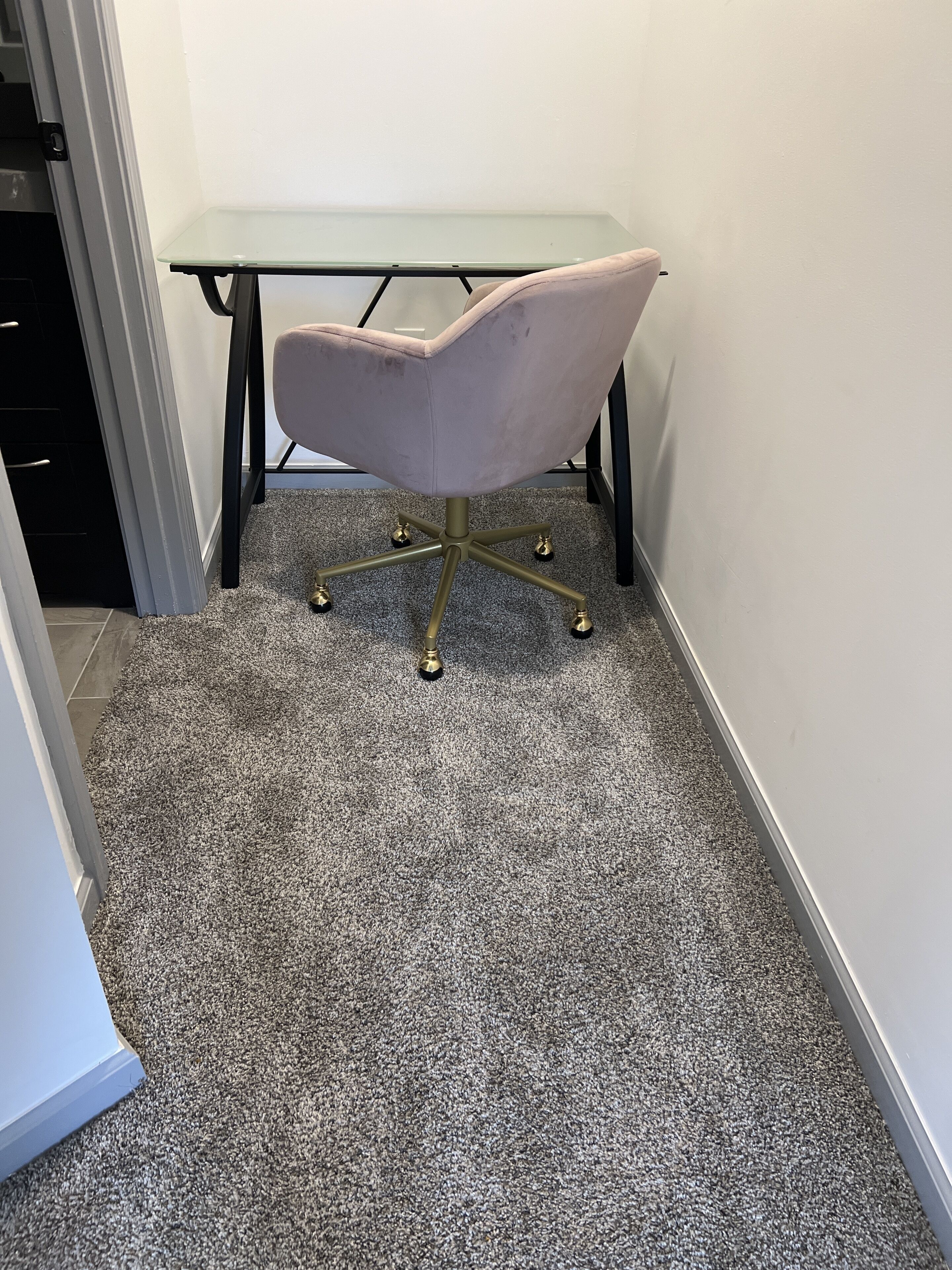 A corner office with a glass desk and a pink chair.